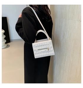 Detailed view of white crossbody bag with quilted heart pattern on a model backdrop