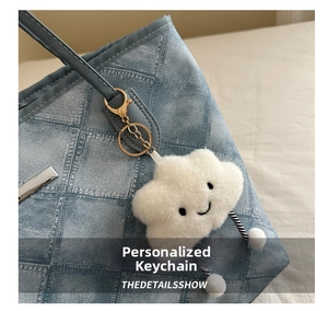 Nahaufnahme eines weißen Plüsch-Wolkenanhängers mit Smiley auf einer blauen Denim-Tasche