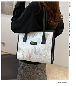 Detail of white quilted tote bag with colorful embroidery and black shoulder strap