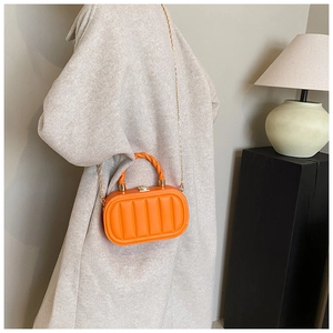 Close-up of bright orange textured small square bag with gold chain and spiral handle