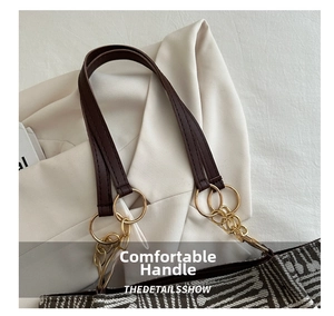 Detail of dark brown leather handle and gold metal ring on a textured jacquard tote bag