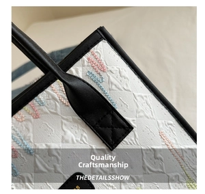 Close-up of white embossed fabric tote bag with colorful embroidery and black leather trim