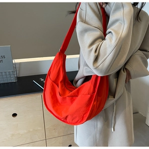 Sac bandoulière demi-lune en nylon rouge vif porté par un mannequin en décor minimaliste