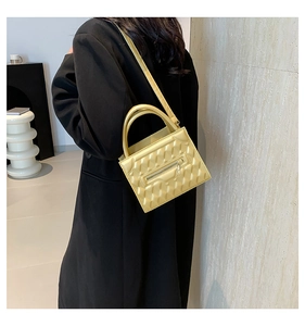 Detail of yellow quilted leather crossbody bag with front zipper and top handle on a model