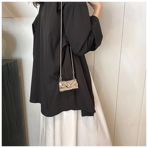 Detail of a conch shell shaped gold metal mini bag with wavy texture and fine chain