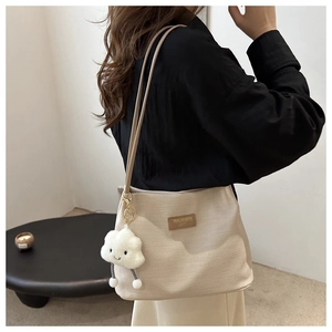 Détail du sac bandoulière en velours côtelé beige avec breloque peluche et logo en cuir
