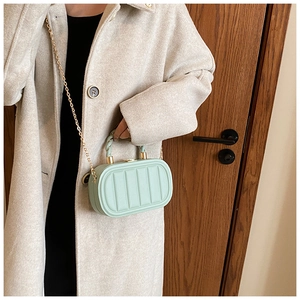 Close-up of mint green handbag with vertical quilted texture and gold chain strap