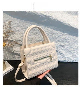 Detail of white quilted crossbody bag with golden zipper and textured geometric pattern