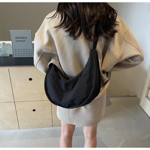 Sac bandoulière demi-lune noir minimaliste porté par un mannequin en intérieur
