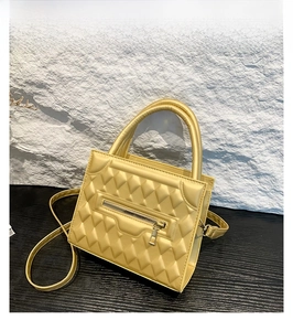Detail of gold quilted crossbody bag featuring a front zipper and chic top handle
