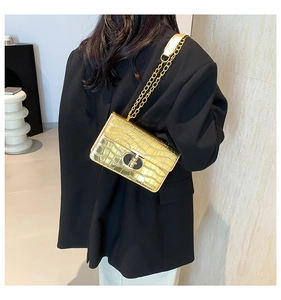 Detailed view of a gold crocodile embossed chain bag worn with a black suit jacket
