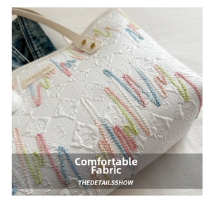 Close-up of quilted tote bag fabric with colorful embroidery and brand label
