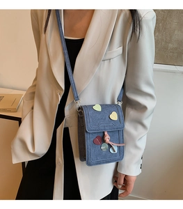 Detail view of denim crossbody bag with rainbow heart patches and tassel on a model