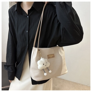 Détail d'un sac cabas beige texturé avec écusson en cuir et breloque nuage en peluche