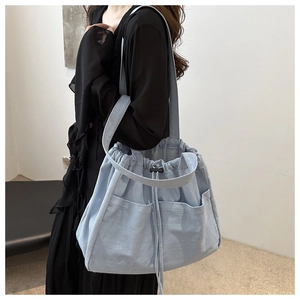 Detail of light blue denim bucket bag showing drawstring closure and large front pockets