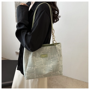 Detail of green striped tote bag with chain strap and leather logo patch on shoulder