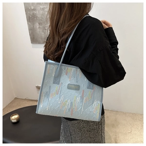 Detail of light blue tote bag featuring colorful wavy stitching and branding on faux leather