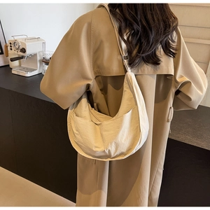 Vue détaillée du sac bandoulière beige en forme de demi-lune porté avec un trench