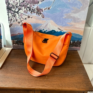 Vibrant orange half-moon crossbody bag with wide adjustable strap on a wooden table