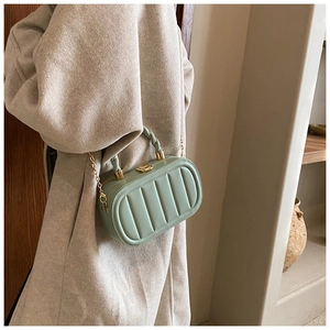 Detail of mint green textured crossbody box bag with gold chain and woven top handle