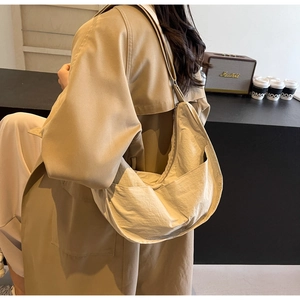 Sac croissant beige en nylon avec bandoulière réglable porté par un mannequin dans un café