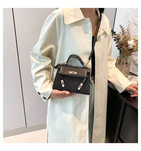 Dettaglio della borsa a tracolla nera glitterata con chiusura dorata su un trench beige