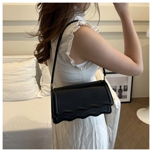 Detail of minimalist black underarm bag featuring a unique triple-layered wavy edge design