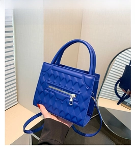 Detail of blue quilted shoulder bag with pyramid texture and silver zipper accent