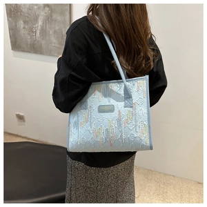 Detail of light blue tote bag with colorful embroidery on a model in a modern interior