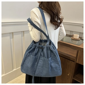 Detail of blue denim drawstring bucket bag with large pockets shown on a model