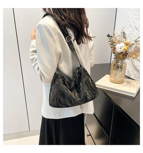 Detail of black pleated shoulder bag with silver buckle and adjustable strap on a model