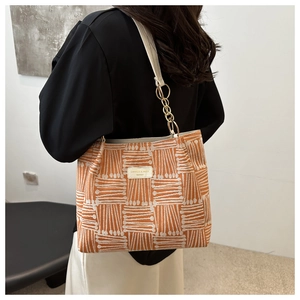 Detailed view of orange and white striped tote bag with leather strap and golden chain