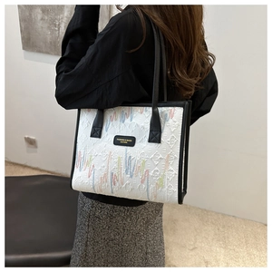 Detail of white textured tote bag with colorful embroidery and black leather handles