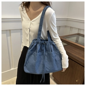 Detail of blue denim tote bag with drawstring closure and two functional front pockets