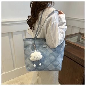 Detail of light blue quilted tote bag with a plush cloud charm and silver logo accent