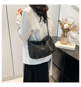 Close-up of a black pleated tote bag with cloud texture and fine strap on white blazer