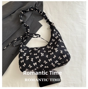 Detail view of black bow-print hobo bag with ruffled strap and smartphone for size reference