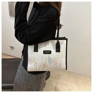 Detail of white tote bag with colorful embroidery and black logo plaque on a shoulder