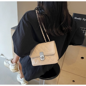 Detail of beige quilted shoulder bag with silver clasp worn by model in minimalist setting
