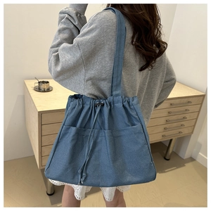Detail of blue denim drawstring bucket bag featuring functional front pockets and shoulder strap