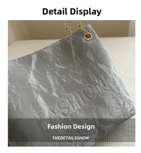 Detail of grey textured shoulder bag with embossed FASHION lettering and gold chain strap