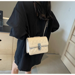 Model wearing a cream quilted crossbody bag with a silver chain strap and metal lock