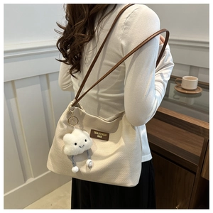 Detail of beige textured shoulder bag with brown leather strap and plush cloud charm