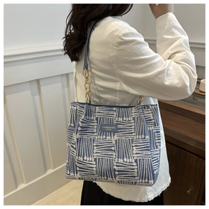 Detail of blue and white striped tote bag with leather logo patch and gold chain strap