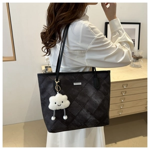 Detail of dark quilted tote bag with a white cloud plush charm and leather shoulder strap