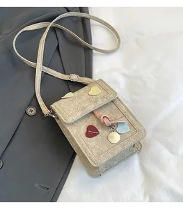 Close-up of beige square crossbody bag featuring colorful heart patches and adjustable strap