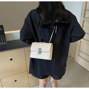 Beige quilted shoulder bag with chain strap shown on model in a home setting