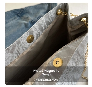 Detail of grey shoulder bag showing golden chain and magnetic snap closure with stone texture