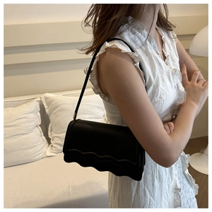 Vue détaillée du sac sous l'aisselle noir minimaliste avec bord ondulé et bandoulière fine