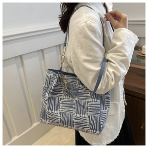 Detail of blue and white striped woven tote bag with leather strap and gold chain accent